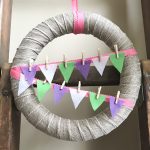 Burlap ribbon wrapped wreath with colorful bunting held on with mini clothes pins