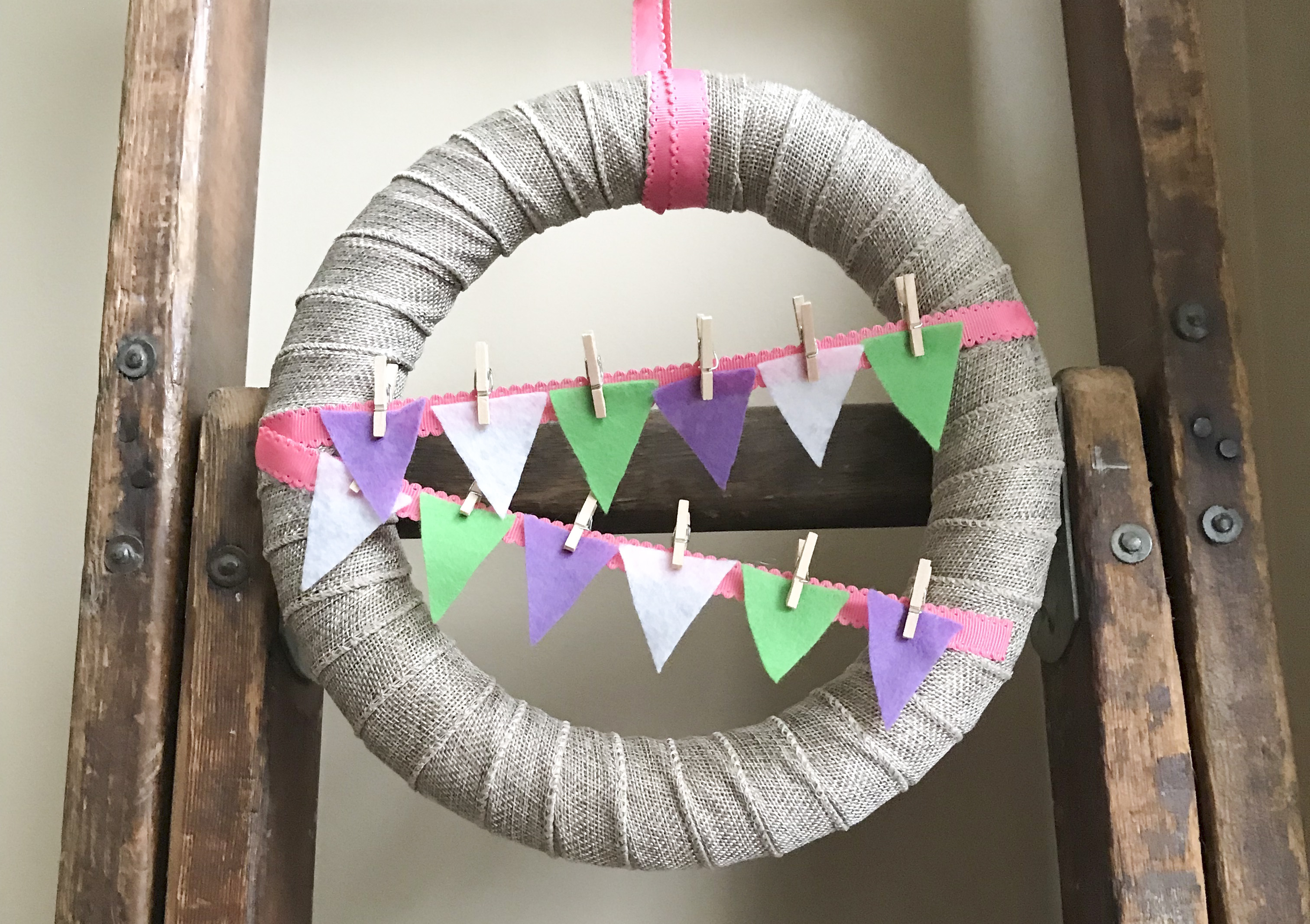 Burlap ribbon wrapped wreath with colorful bunting held on with mini clothes pins